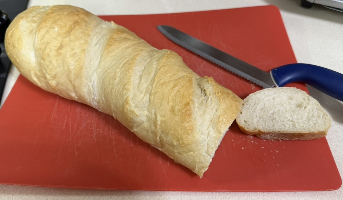 A golden French bread loaf on a cutting board, sliced to show the soft open interior
